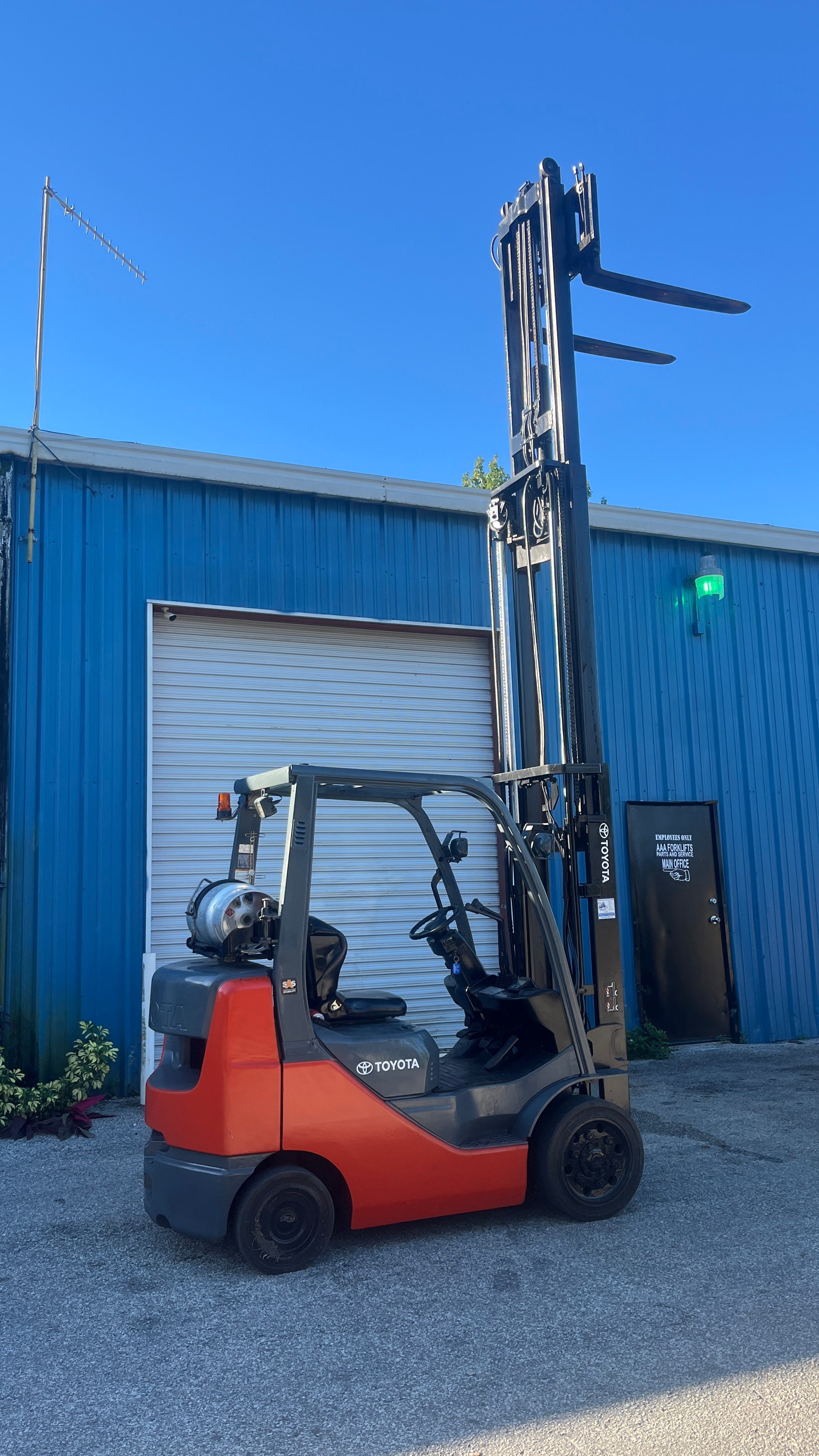 Orange and black forklift parked in front of a blue building with a clear blue sky.
